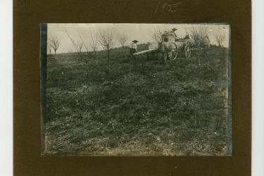 Black man sat atop a horse-drawn cart, spraying fields while two Black men follow behind