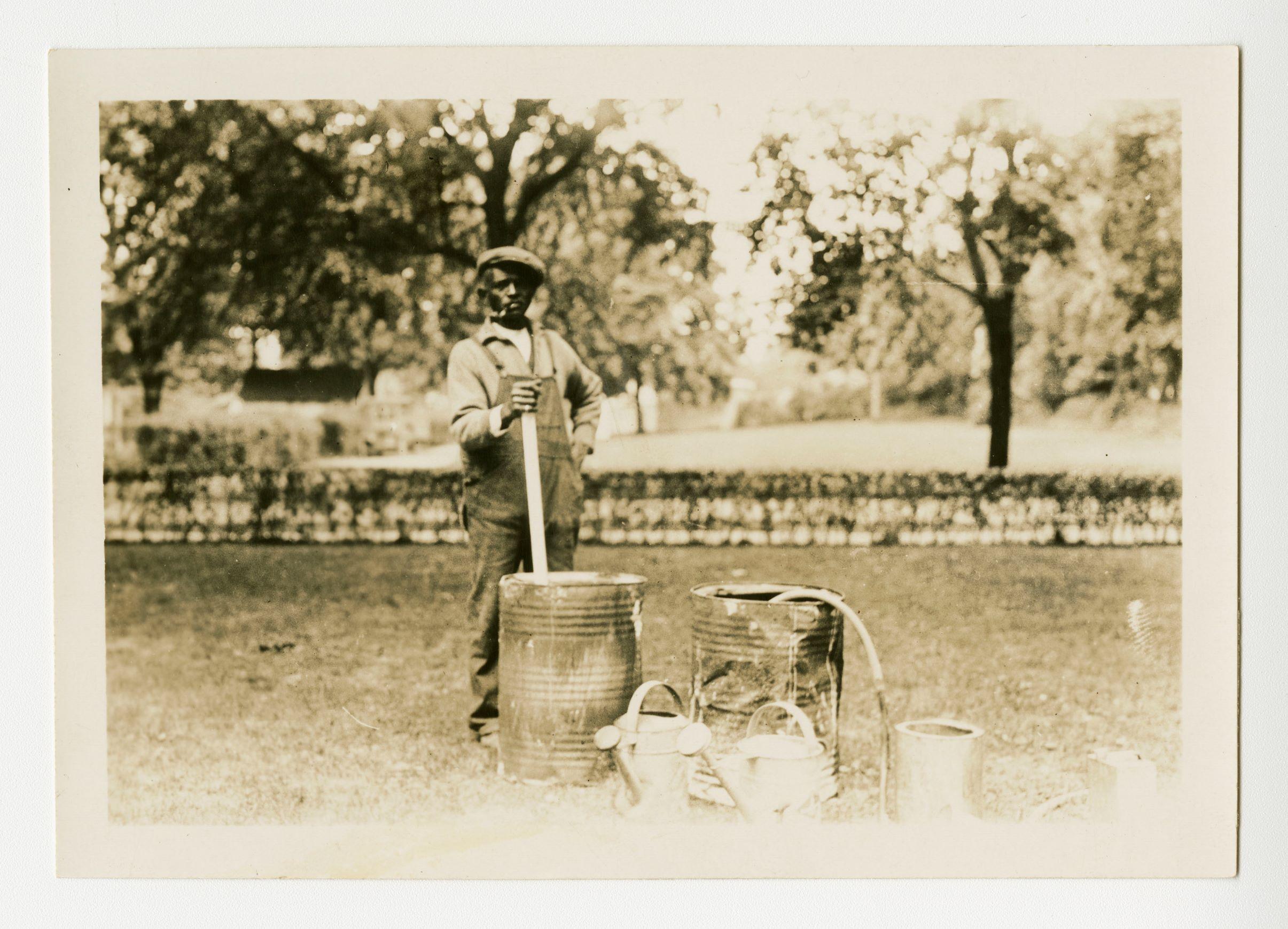 Black man standing with barrels and watering cans