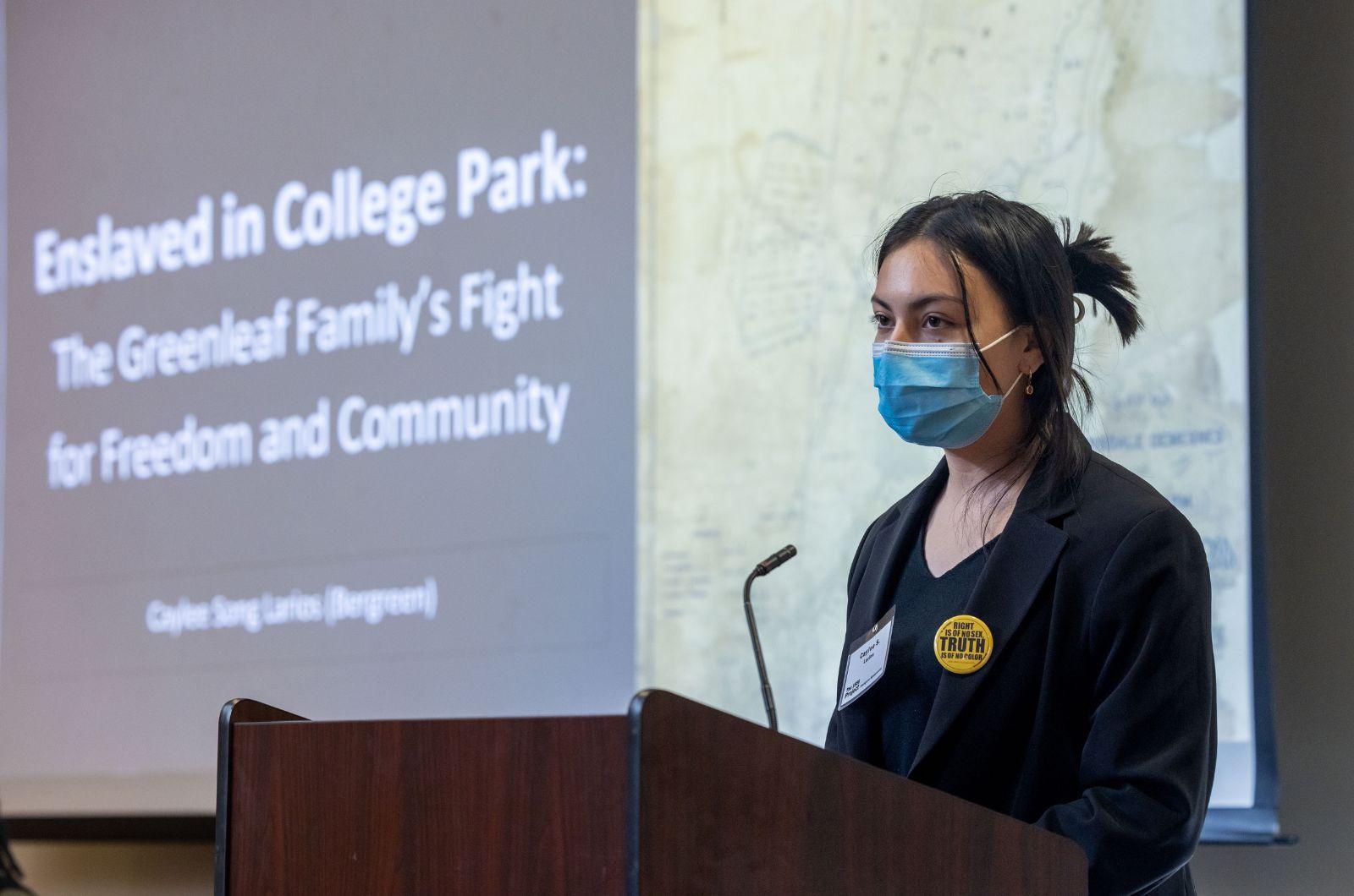 Caylee Song Bergreen standing at a podium in front of her presentation, "Enslaved in College Park: The Greenleaf Family's Fight for Freedom and Community"