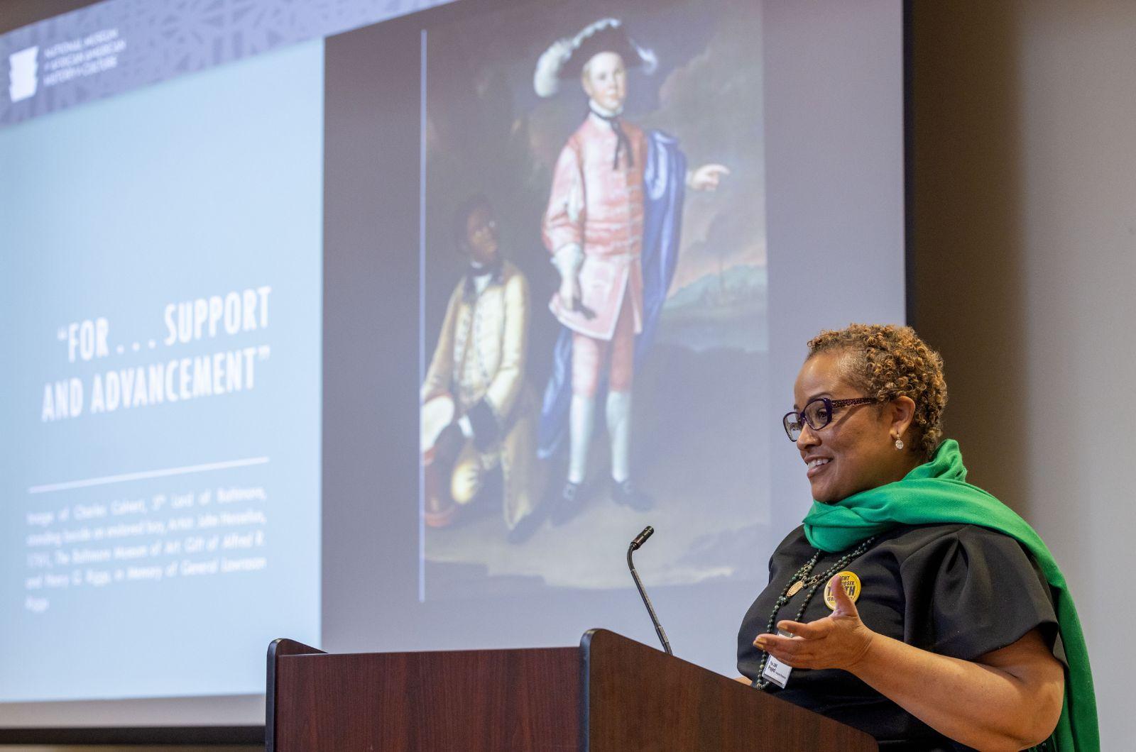 Mary Elliott standing at the podium in front of her slide presentation